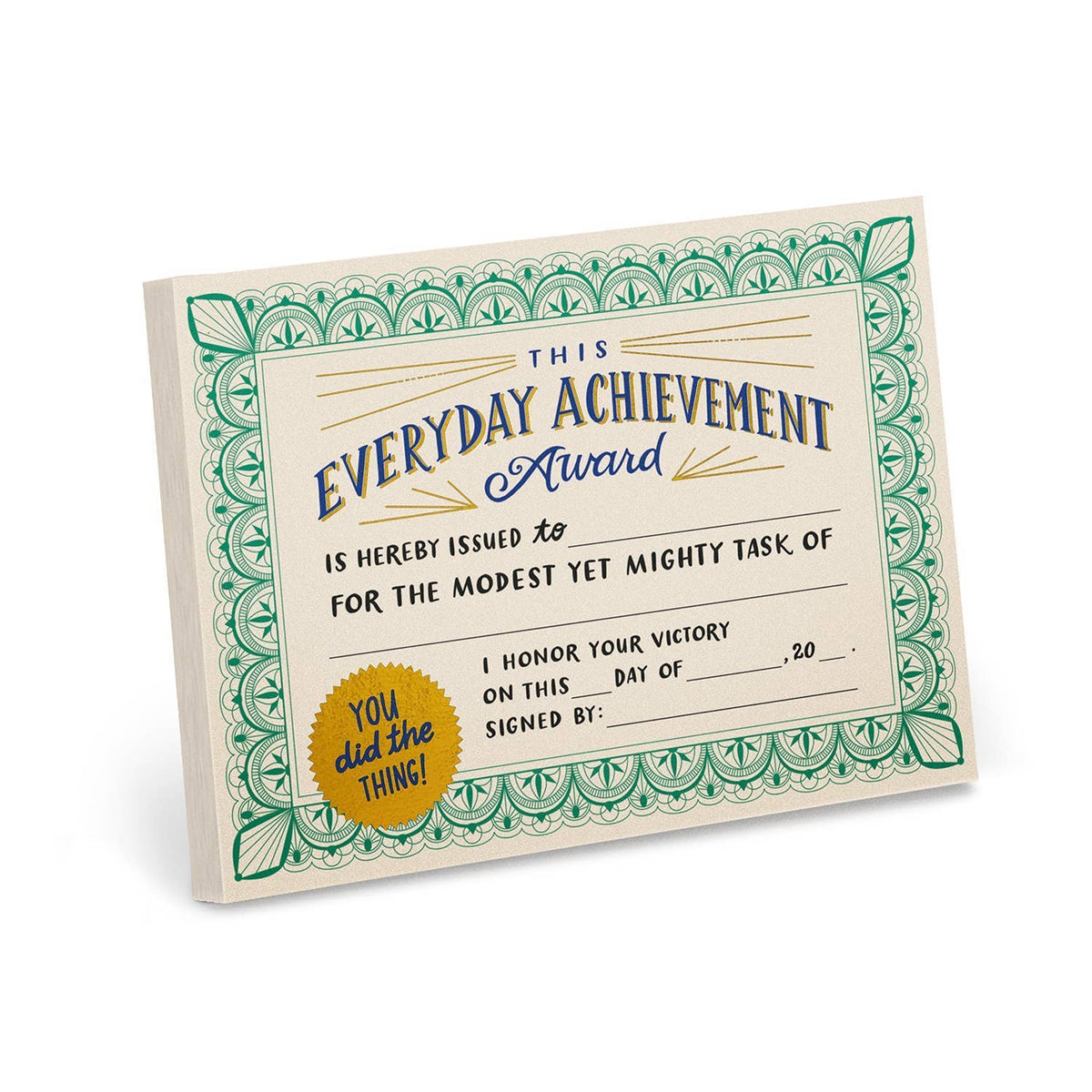 Everyday Achievement Award Certificate Notepad by Em & Friends — cream notepad with ornate green border, bold blue and gold foil title reading "This Everyday Achievement Award is hereby issued to for the modest yet mighty task of ," gold seal reading "You did the thing!" and fill-in lines for date and signature, shown at an angle on a white background