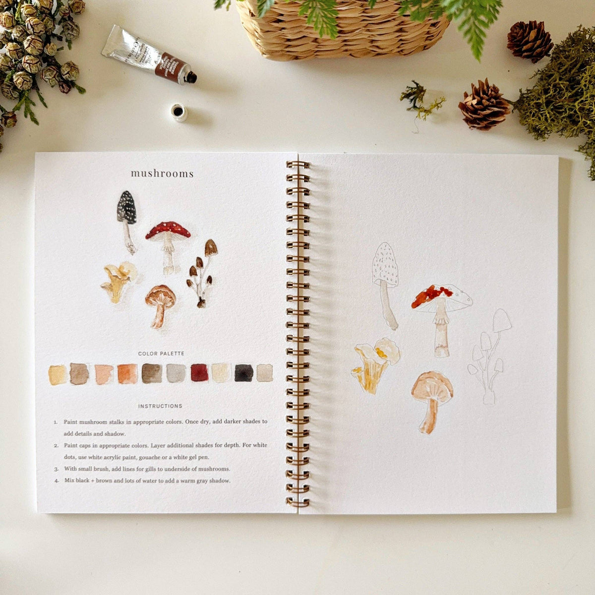 Open spread of Woodland Watercolor Workbook showing mushrooms illustration with color palette and instructions on left, partially painted mushroom sketches on right