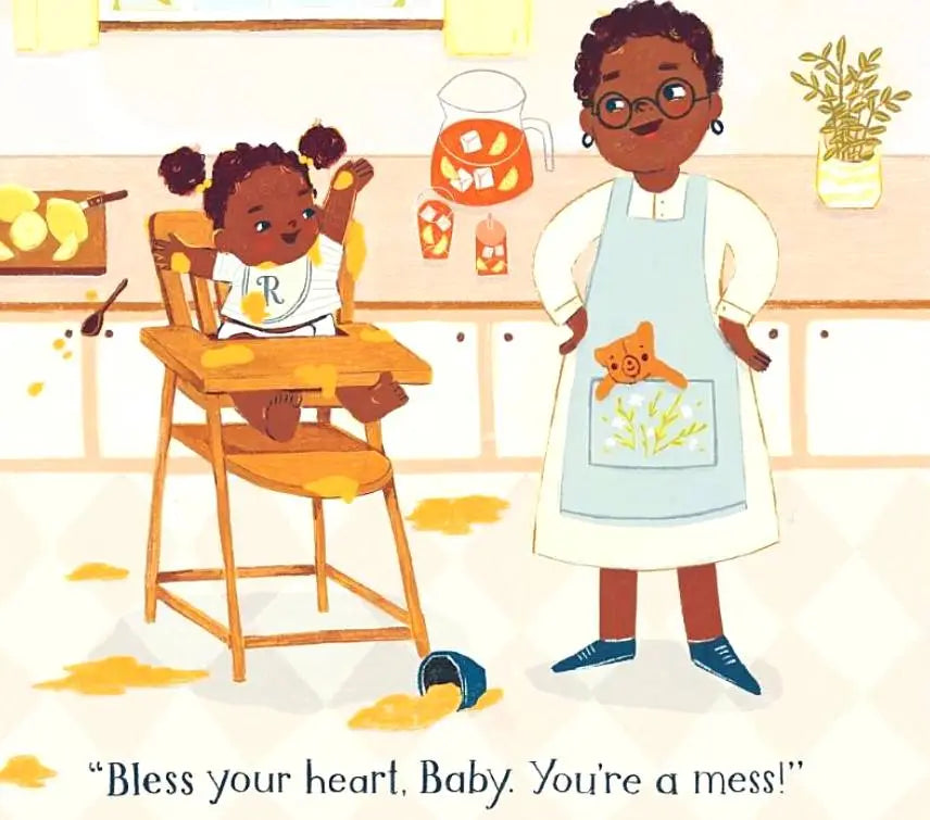 Interior page from Southern Baby board book — cozy kitchen illustration of a grandmother in a blue apron standing beside a baby in a high chair who has made a mess with food, a pitcher of sweet tea on the counter, and the text "Bless your heart, Baby. You're a mess!"