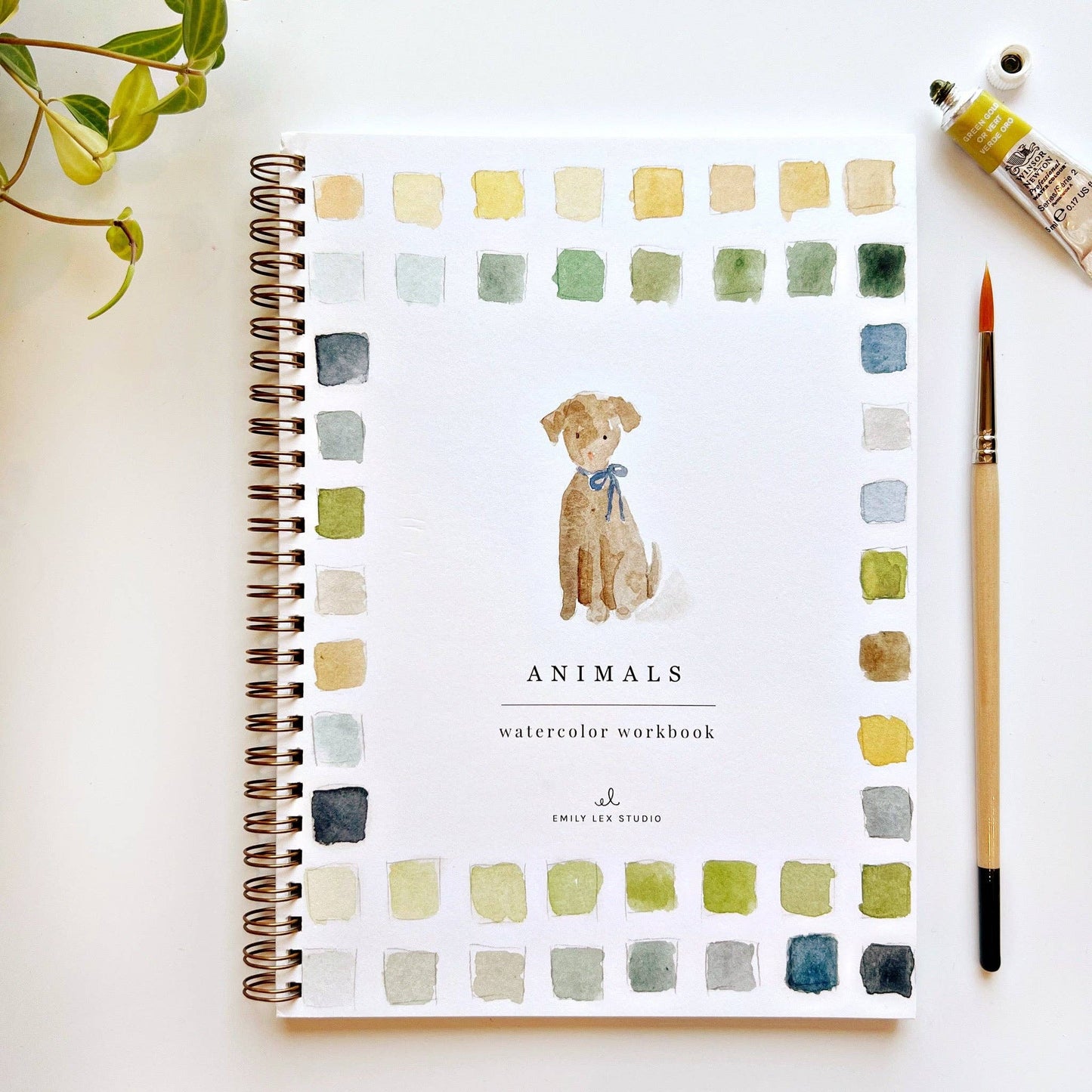 Emily Lex Studio Animals Watercolor Workbook cover with a golden puppy illustration surrounded by watercolor paint swatches in greens, blues, and tans, styled with a paintbrush and watercolor tube on a white surface