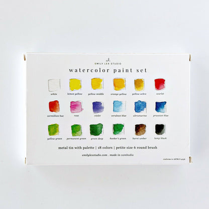 Emily Lex Studio watercolor paint set box back on white surface; shows all 18 colors labeled in three rows of 6 with watercolor swatches; "metal tin with palette | 18 colors | petite size 6 round brush · emilylexstudio.com · made in cambodia · conforms to ASTM D 4236" text at bottom; Emily Lex Studio logo at top


