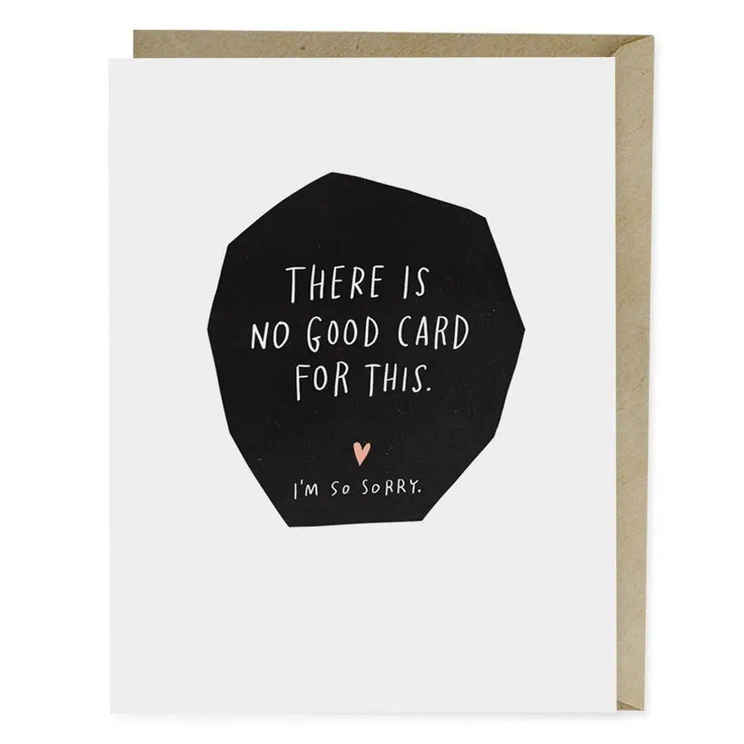 White A2 sympathy card by Em & Friends leaning against a kraft envelope — bold black irregular polygon shape in the center with white hand-lettered text reading "THERE IS NO GOOD CARD FOR THIS." and a small pink heart below with "I'm So Sorry." in delicate script, on a white background