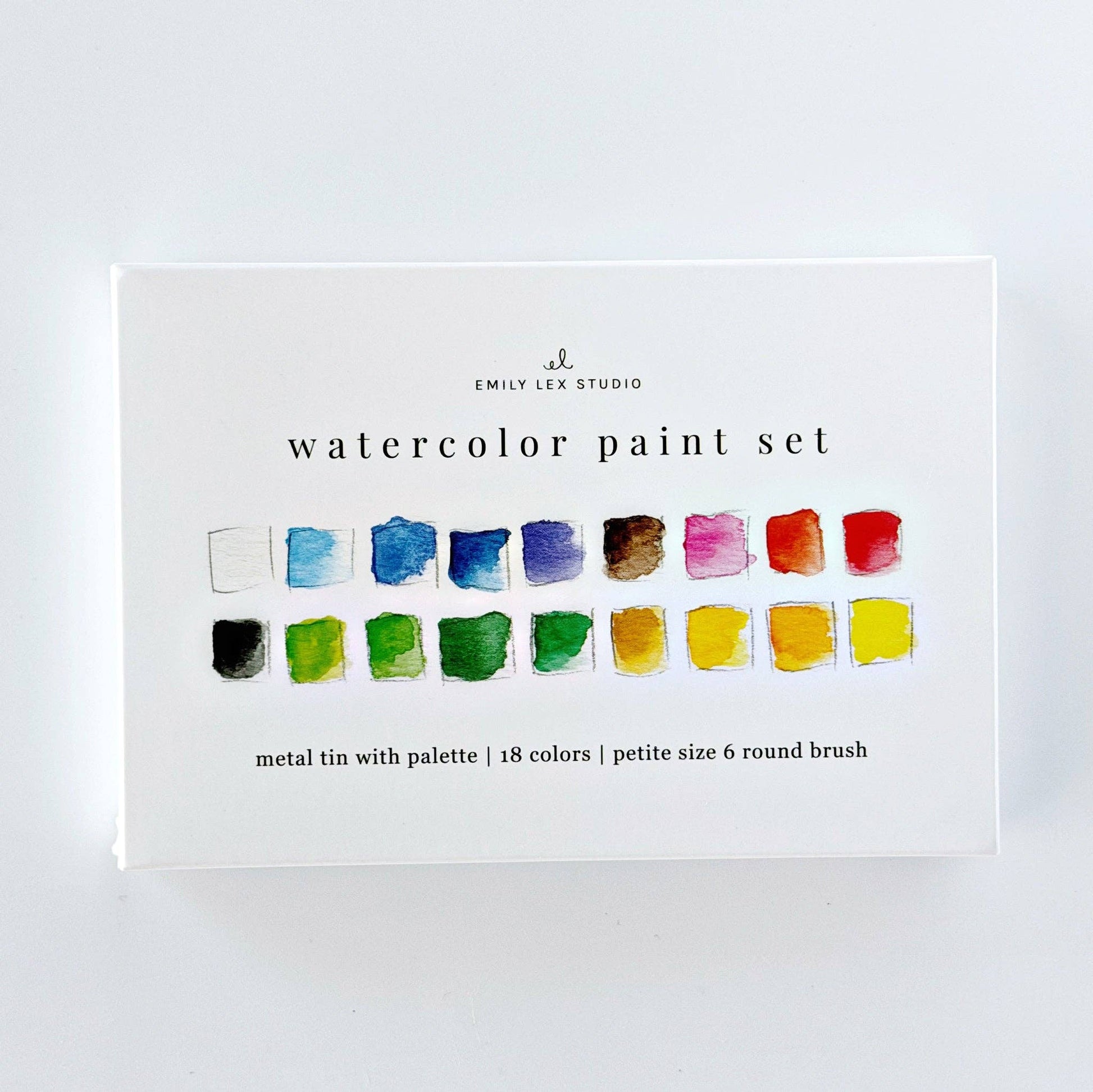  Emily Lex Studio watercolor paint set box standing upright on white surface; front shows 18 watercolor swatches in two rows and "watercolor paint set · metal tin with palette | 18 colors | petite size 6 round brush" text; Emily Lex Studio logo at top