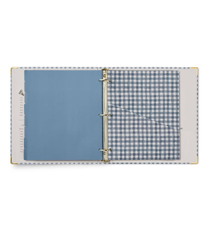 Rifle Paper Co. Home Sweet Home Recipe Binder open showing dusty blue tabbed divider page on left and clear gingham-print pocket page on right; gold ring binding and corner accents visible