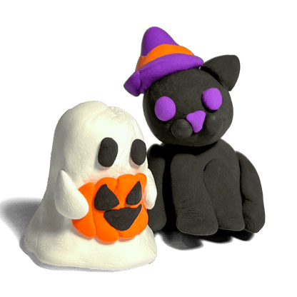 Close-up of two completed OOLY Creatibles Spooky BFFs air dry clay figurines on white background — friendly ghost holding an orange jack-o-lantern and a black cat wearing a purple and orange witch hat