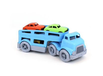 Green Toys Car Carrier on white background — blue double-decker transport truck viewed from the front-right with ramps up and all three Mini Cars loaded; orange Mini Car and green Mini Car on the upper deck; yellow Mini Car partially visible in the lower enclosed deck; chunky blue cab with grey ribbed grille and six grey wheels
