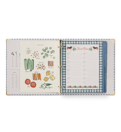 Rifle Paper Co. Home Sweet Home Recipe Binder open to Knife Cuts illustrated reference page on left showing mince, brunoise, julienne, and slice cuts; Favorite Meals fill-in page with cow and floral border on right; blue tabbed dividers visible