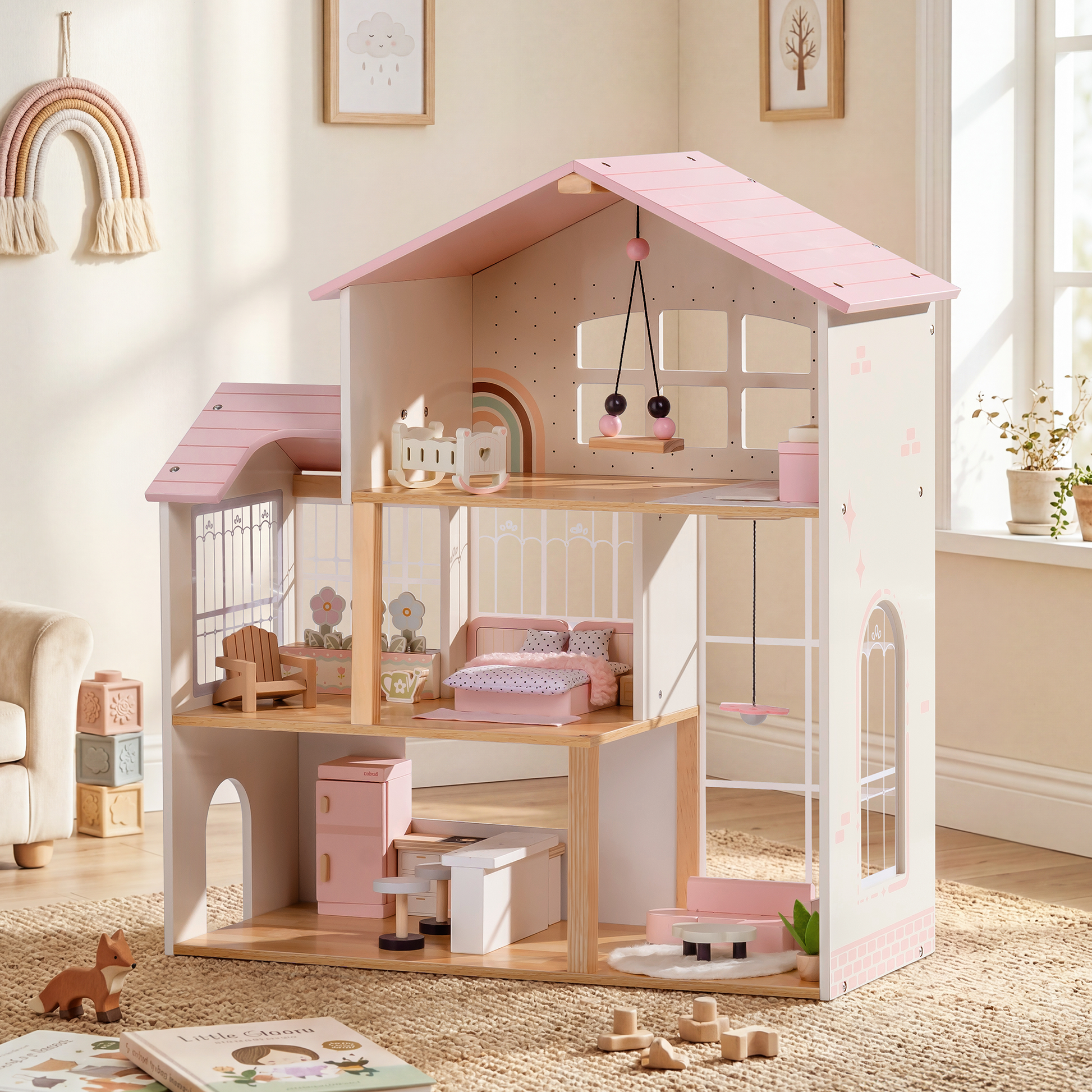 Robud 3-story pink and cream wooden dollhouse in a sunlit Scandinavian children's room — framed botanical prints on white walls; tower sunroom with lattice window on left; children's room, bedroom, and kitchen across 3 floors; loose wooden toys and a children's book on the floor in the foreground