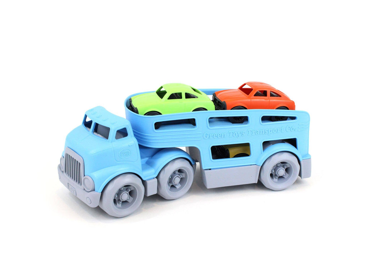 Green Toys Car Carrier on white background — blue double-decker plastic transport truck viewed from the front-left; green and orange Mini Cars loaded on the upper deck; yellow Mini Car visible through the lower deck window; grey cab with ribbed grille, blue cab-over body, and six grey wheels on the tractor-trailer; Green Toys Car Carrier embossed on the trailer side rail