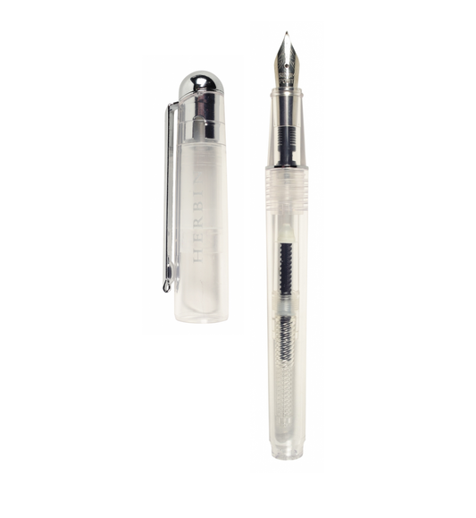 J. Herbin Demonstrator fountain pen on white background — clear transparent barrel with piston converter and dark ink residue visible inside; steel iridium nib with silver-tone section and grip; cap removed and placed to left showing silver dome finial, clip, and frosted body with embossed Herbin text