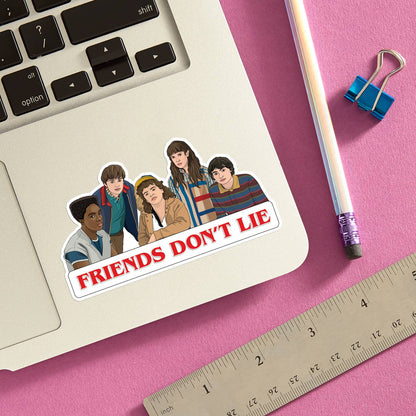 Stranger Things Friends Don't Lie die cut vinyl sticker by The Found styled on a laptop trackpad against a pink background alongside a pencil, ruler, and binder clip