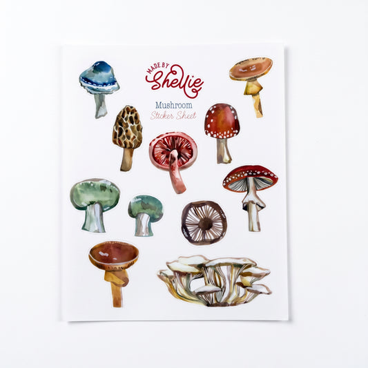 Made by Shellie Mushroom Sticker Sheet — ten watercolor mushroom stickers including blue-capped, morel, fly agaric, red-spotted toadstool, green-capped, brown-gilled, and oyster mushroom cluster; white sheet with Made by Shellie logo; white background