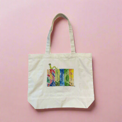 Natural canvas tote bag with watercolor Harry Potter book spine illustration on a pink background, full bag view showing handles and gusset