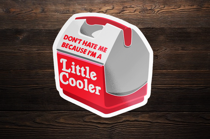 Sticker Bull Don't Hate Me Because I'm A Little Cooler die cut vinyl sticker centered on a dark horizontal wood plank background — illustrated red and gray mini lunchbox cooler with red and white pun text; white die cut border