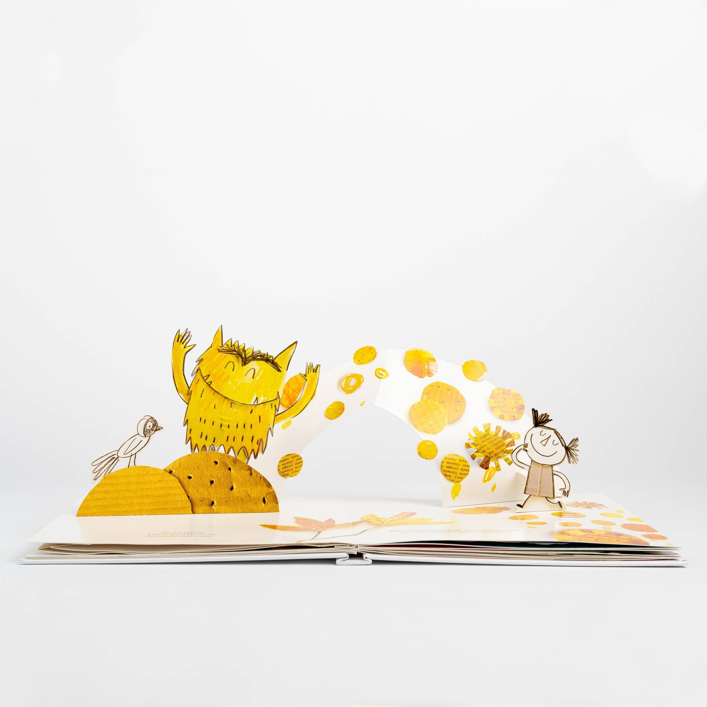 Open spread of The Color Monster: A Pop-Up Book of Feelings showing the happiness page — 3-D pop-up of a golden yellow monster with arms raised joyfully on a sunny hill with a bird, yellow polka dot burst arching across to the sketched girl holding a yellow flower, on a white background
