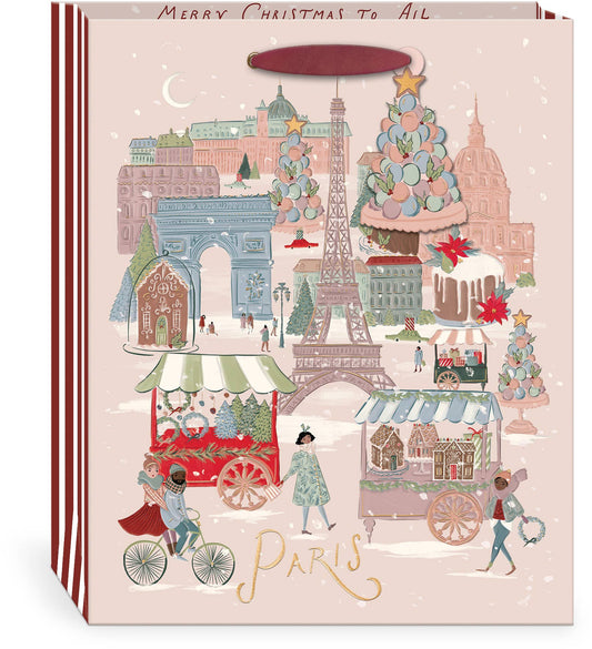 Punch Studio Joy to the World Paris Christmas large gift bag on white background — blush ground with detailed illustrated winter Paris scene: Eiffel Tower, Arc de Triomphe, and Haussmann buildings in snowfall; Christmas market carts with wreath and gingerbread sellers; figures cycling and strolling; decorated macaron and layer cake towers; gold foil script "Paris" at bottom; "Merry Christmas to All" text along top border; red and white striped sides; deep cranberry ribbon handle