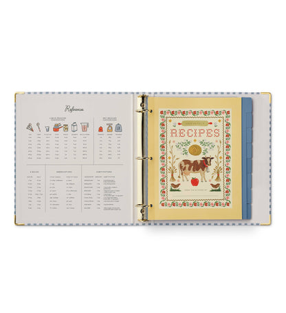 Rifle Paper Co. Home Sweet Home Recipe Binder open to References page showing liquid and dry measure conversions, abbreviations, and substitutions on left; illustrated Recipes cover page with cow and floral border on right; blue tabbed dividers visible