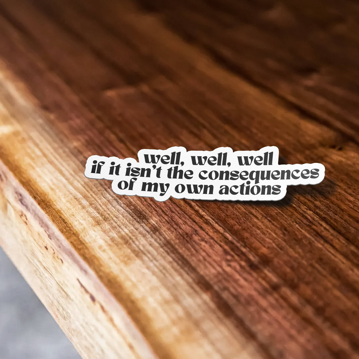 Sticker Bull Well Well Well If It Isn't the Consequences of My Own Actions funny vinyl sticker laid on a warm wood surface at an angle — black retro serif lettering with white die cut border