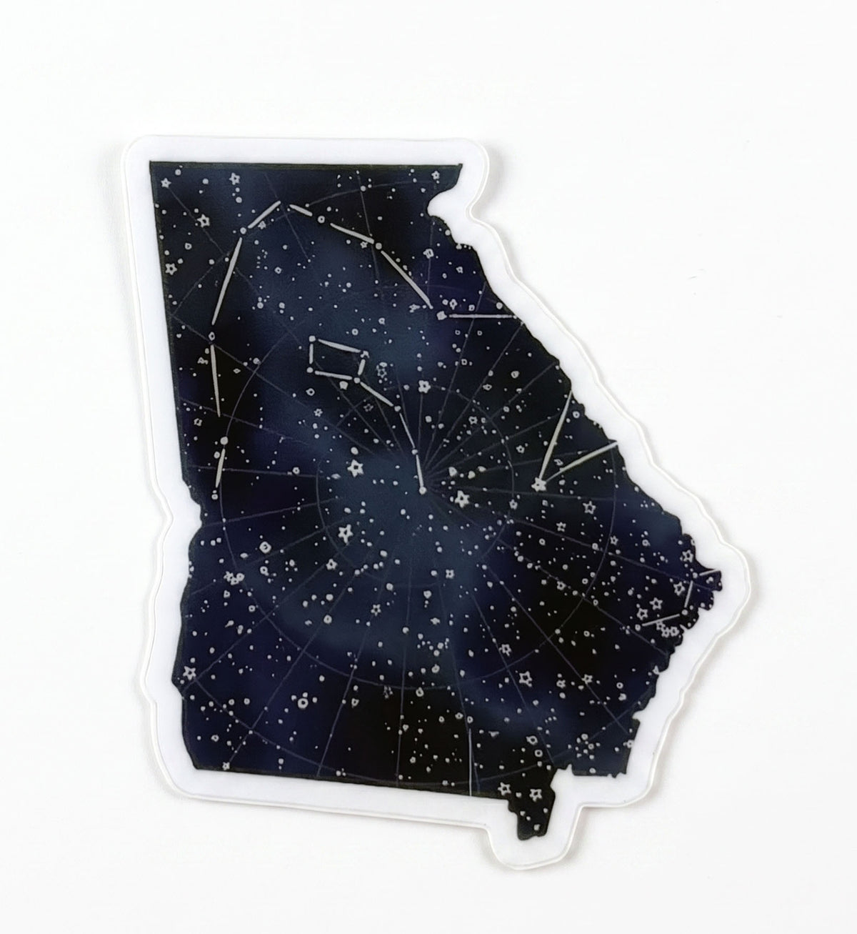Made by Shellie Georgia Constellations vinyl sticker — Georgia state silhouette filled with a deep navy night sky, scattered stars, and constellation lines mapped across the state shape; die-cut with white border; white background