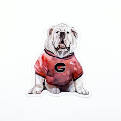 Made by Shellie Sitting Bulldog in UGA Jersey vinyl sticker — watercolor white English bulldog sitting upright in a red UGA jersey with bold black "G" on the chest; die-cut with white border; white background