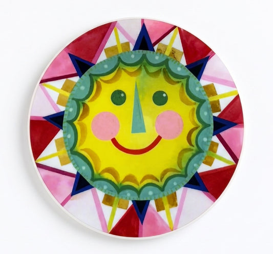 Made by Shellie Yellow Sun vinyl sticker — bold retro smiling sun face in yellow with teal scalloped border, pink rosy cheeks, green eyes, and teal triangular nose surrounded by geometric starburst rays in reds, pinks, navy, and gold; round with white border; white background