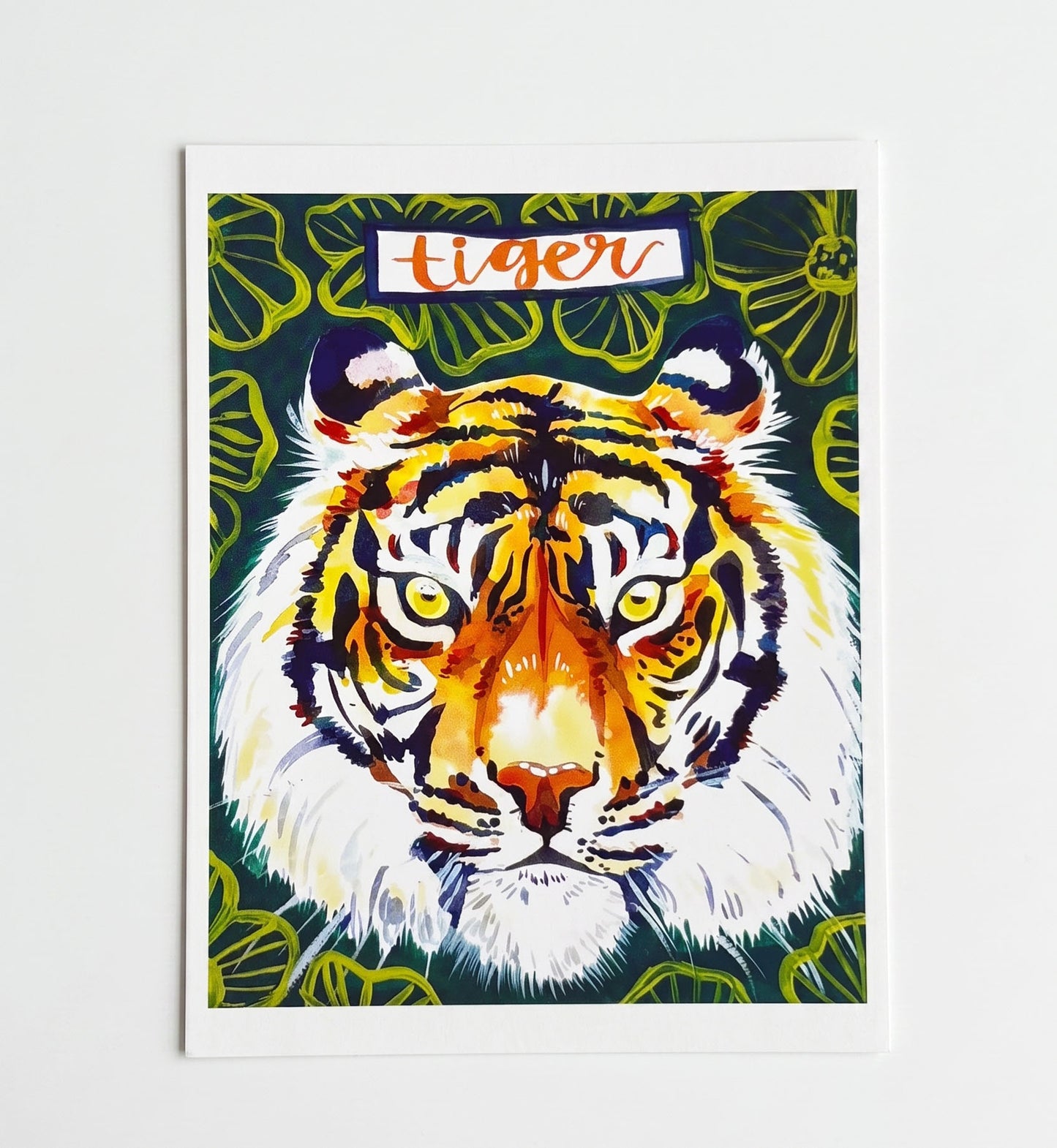 Made by Shellie Tiger Art Print — illustrated tiger face with orange, gold, and black stripes surrounded by green tropical foliage with "tiger" in orange script lettering at top; white background